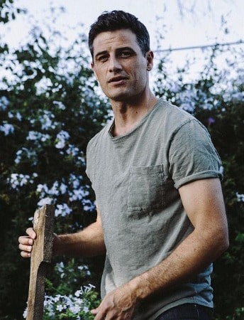 Picture of Enver Gjokaj in a white t shirt with a nice nature background.